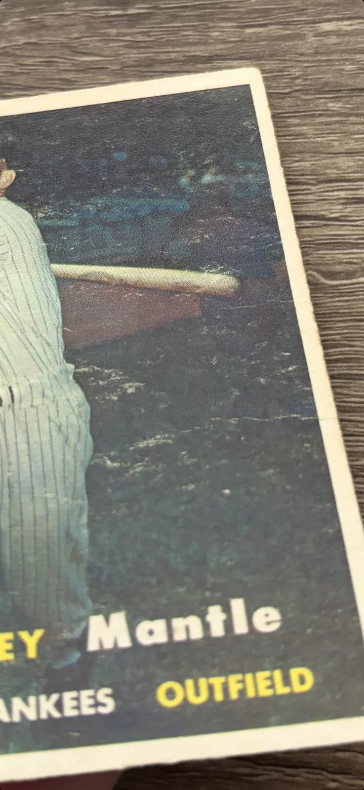 Side-lit front surface of the 1957 Topps Mickey Mantle #95, raking light revealing surface wear and a diagonal crease running through the lower-right corner